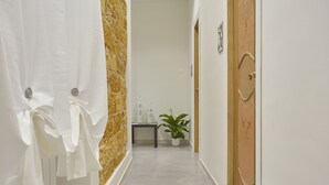 A hallway with a white door on the left, a wooden door on the right, and a plant in the center. - Better & Better (Palermo)