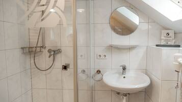 Een moderne badkamer met een douchecabine van glas, een wit wastafeltje, een ronde spiegel en een dakraam.
