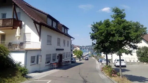 A street view with a white building featuring a balcony and a small outdoor seating area. - Gasthaus Hotel Anker (Konstanz)