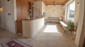 A spacious room with a wooden ceiling, a built-in kitchen counter, a seating area with a bench, and a large window providing natural light. - Masseria Chinunno (Altamura)