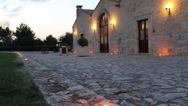 A stone building with a paved courtyard, a lit candle, and wall-mounted lights. - Masseria Chinunno (Altamura)