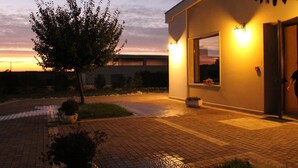 A modern building with a large window and a door, surrounded by a paved area with potted plants. - Masseria Chinunno (Altamura)