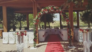 An outdoor wedding arch with white chairs and a red carpet, surrounded by greenery. - Masseria Chinunno (Altamura)