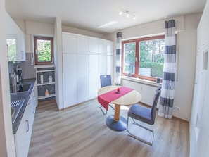 A compact kitchen with modern appliances, a dining area with a table and chairs, and a window with curtains.