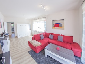 A modern living room with a red sofa, a coffee table, and a kitchen area in the background.