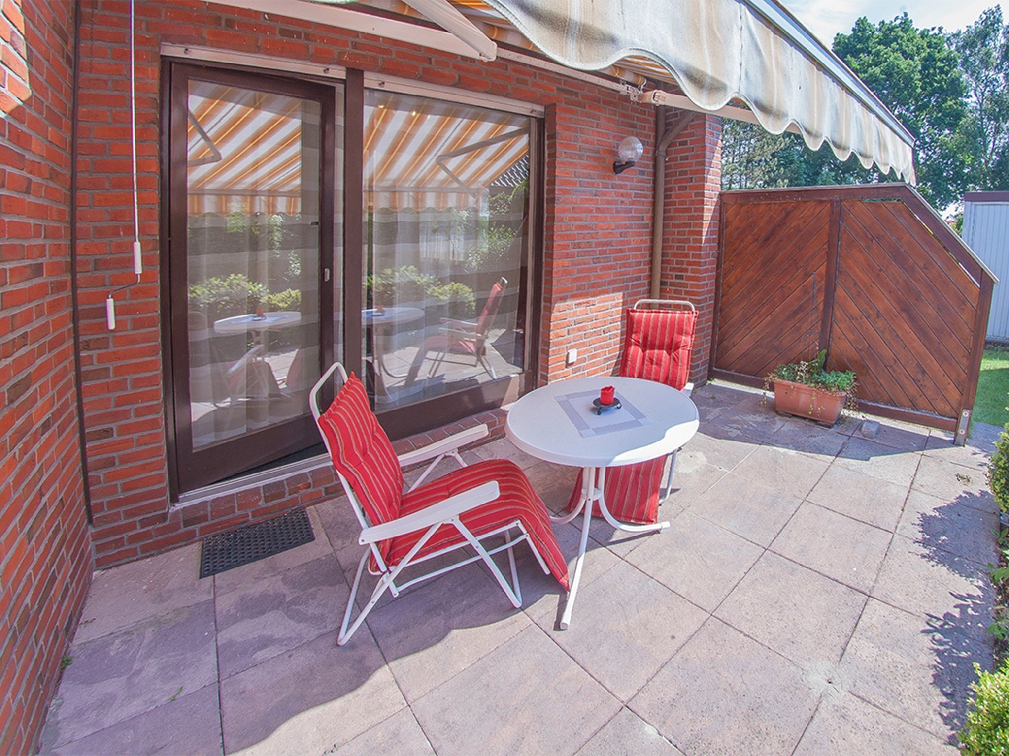 A patio with a table and two chairs, a sliding glass door, and a wooden fence.