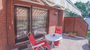 Une terrasse avec une table et deux chaises, une porte-fenêtre coulissante et une clôture en bois.