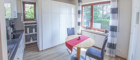 A compact kitchen with modern appliances, a dining area with a table and chairs, and a window with curtains.