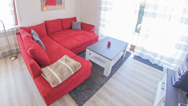 Un canapé rouge, une petite table, un tapis et un tableau accroché au mur.