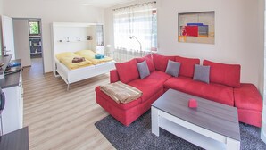Un salon moderne avec un canapé rouge, un lit blanc et une petite table.