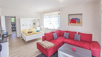 A modern living room with a red sofa, a white bed, and a small table.