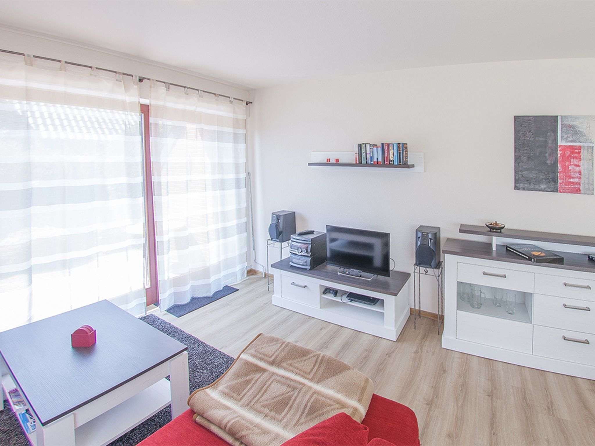 A modern living room with a flat-screen TV, a coffee table, a sofa, a dining table, and a kitchen area with a countertop and cabinets.
