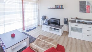 Un salon moderne comprenant un téléviseur à écran plat, une table basse, un canapé, une table à manger et un coin cuisine avec un plan de travail et des placards.