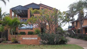 A two-story house with a brick facade, a covered patio, and a well-maintained garden with palm trees and shrubs. - 'Horizons' Unit 2 - Beachfront Unit (BARGARA)