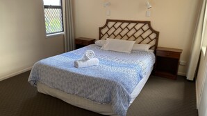 A neatly made bed with a patterned bedspread and a rolled towel, wooden headboard, bedside tables, and a window with curtains. - 'Horizons' Unit 2 - Beachfront Unit (BARGARA)