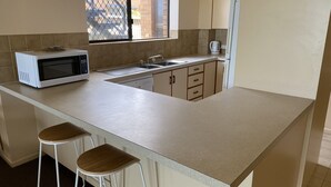 A kitchen with a microwave, sink, and two stools. - 'Horizons' Unit 2 - Beachfront Unit (BARGARA)