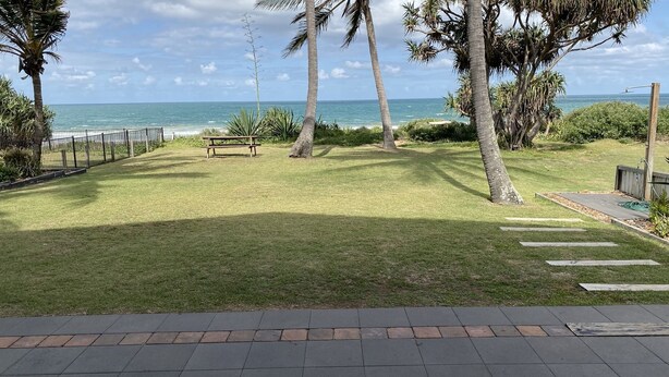 A grassy outdoor area with a bench and a view of the ocean. - 'Horizons' Unit 2 - Beachfront Unit (BARGARA)