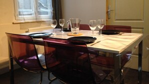Une table à manger dressée avec des assiettes, des couverts et des verres, entourée de chaises transparentes.