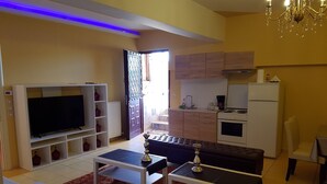 Sala de estar com televisão, sofá, mesa de centro e cozinha com armários e eletrodomésticos.