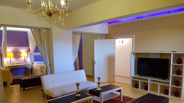 Uma sala de estar moderna com um sofá branco, uma mesa de centro, uma televisão sobre um suporte branco e um candelabro.