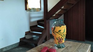 A rustic wooden table with a decorative vase and a pair of red slippers. A staircase with wooden railings is visible in the background. - MammaColette (Marsala)