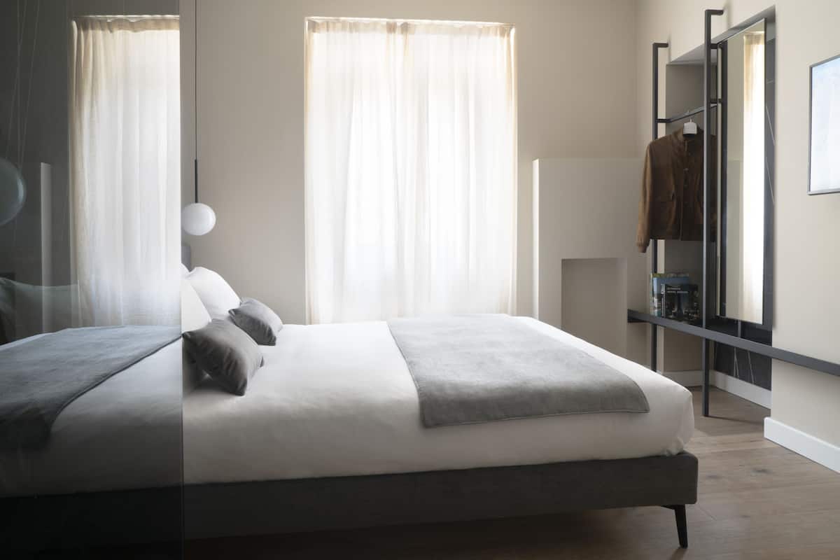 Een moderne slaapkamer met een groot bed, nachtkastje, kledingkast en een raam met dunne gordijnen.