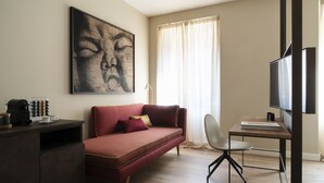Un salon moderne avec un canapé rouge, une table basse, un bureau avec une chaise, un grand téléviseur à écran plat et une fenêtre ornée de rideaux légers.