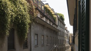 Une rue étroite en milieu urbain, bordée de bâtiments des deux côtés, avec des balcons ornés de plantes et un trottoir pour les piétons.
