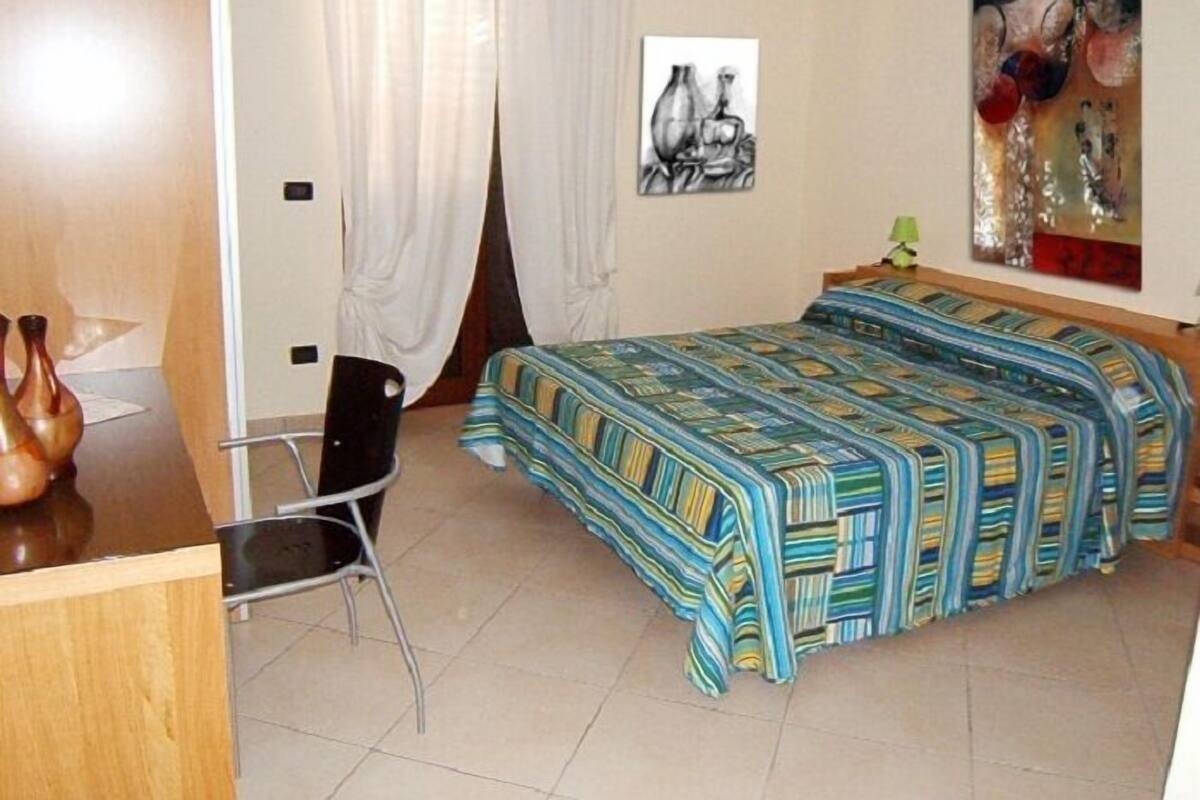 A bedroom with a bed, a chair, a desk, and a painting on the wall.