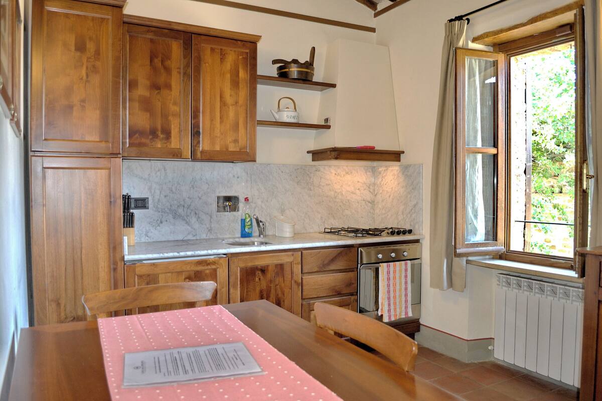 A kitchen with wooden cabinets, a gas stove, a sink, and a window with curtains.