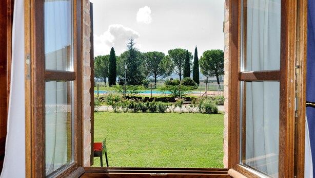 Una puerta abierta que da a un espacio exterior con césped, árboles y una piscina.