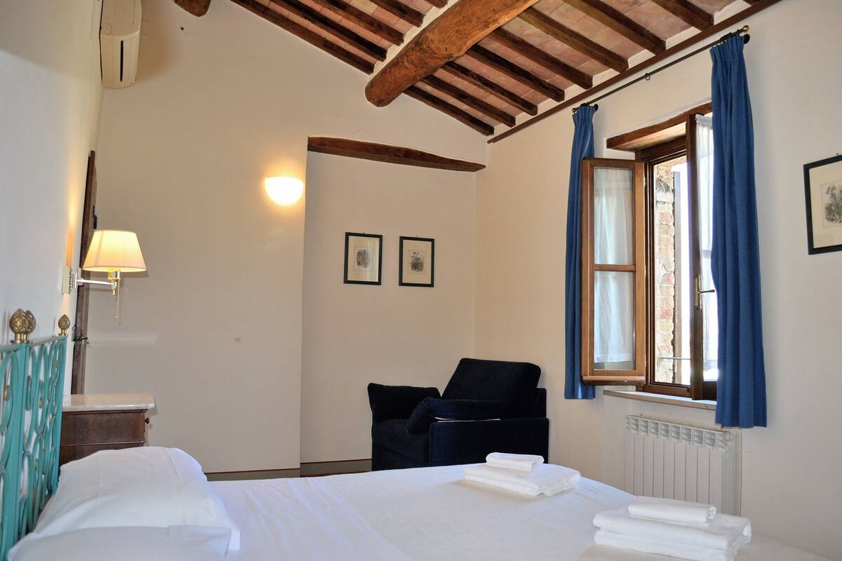 A hotel room with a bed, a chair, a desk, and a window with curtains.