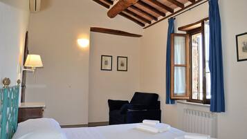A hotel room with a bed, a chair, a desk, and a window with curtains.