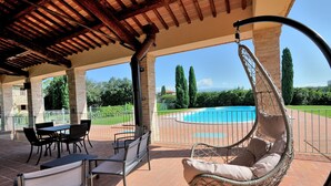 Un patio exterior con una silla colgante, una mesa con sillas y vistas a una piscina.