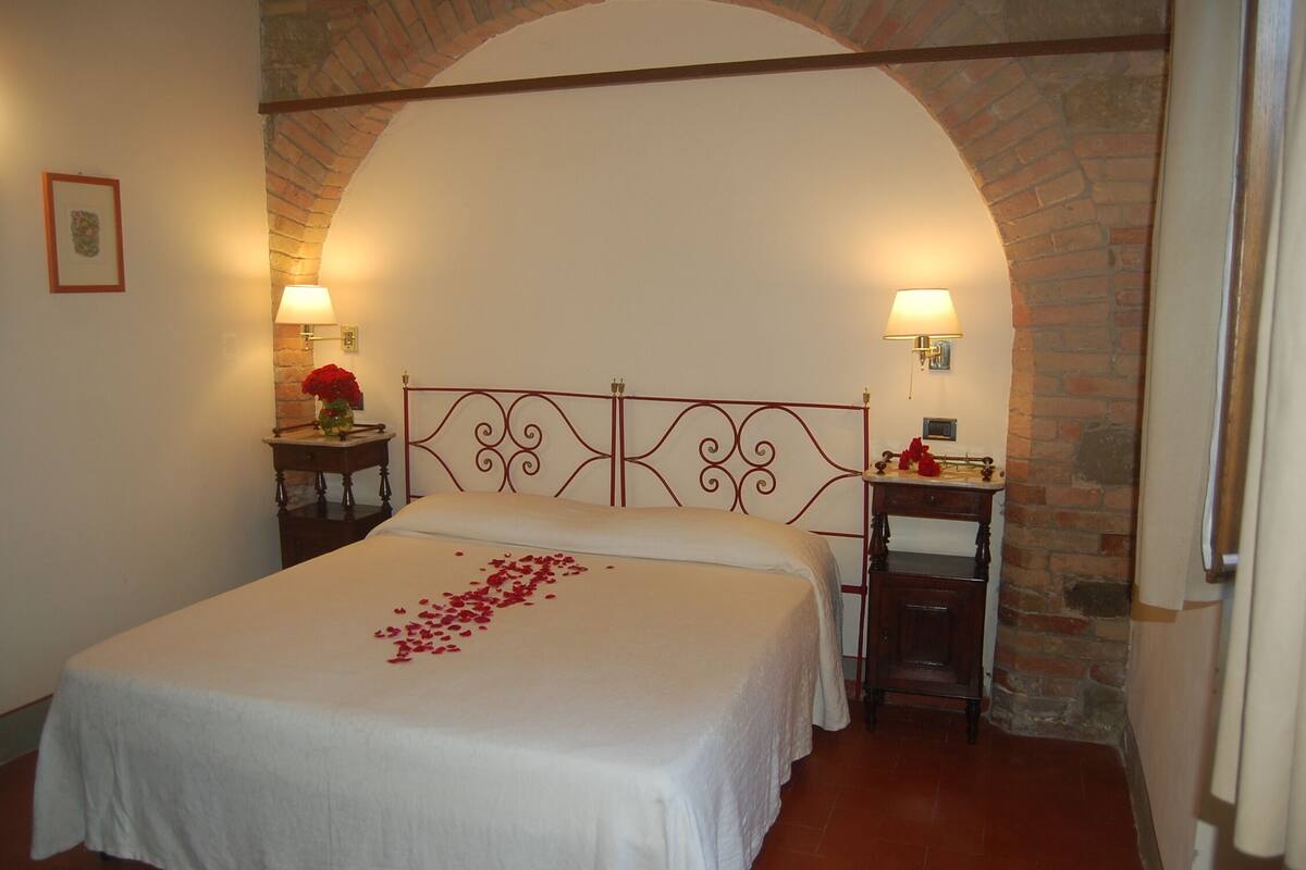 A room with a large bed, two bedside tables, a brick archway, and a framed picture on the wall.