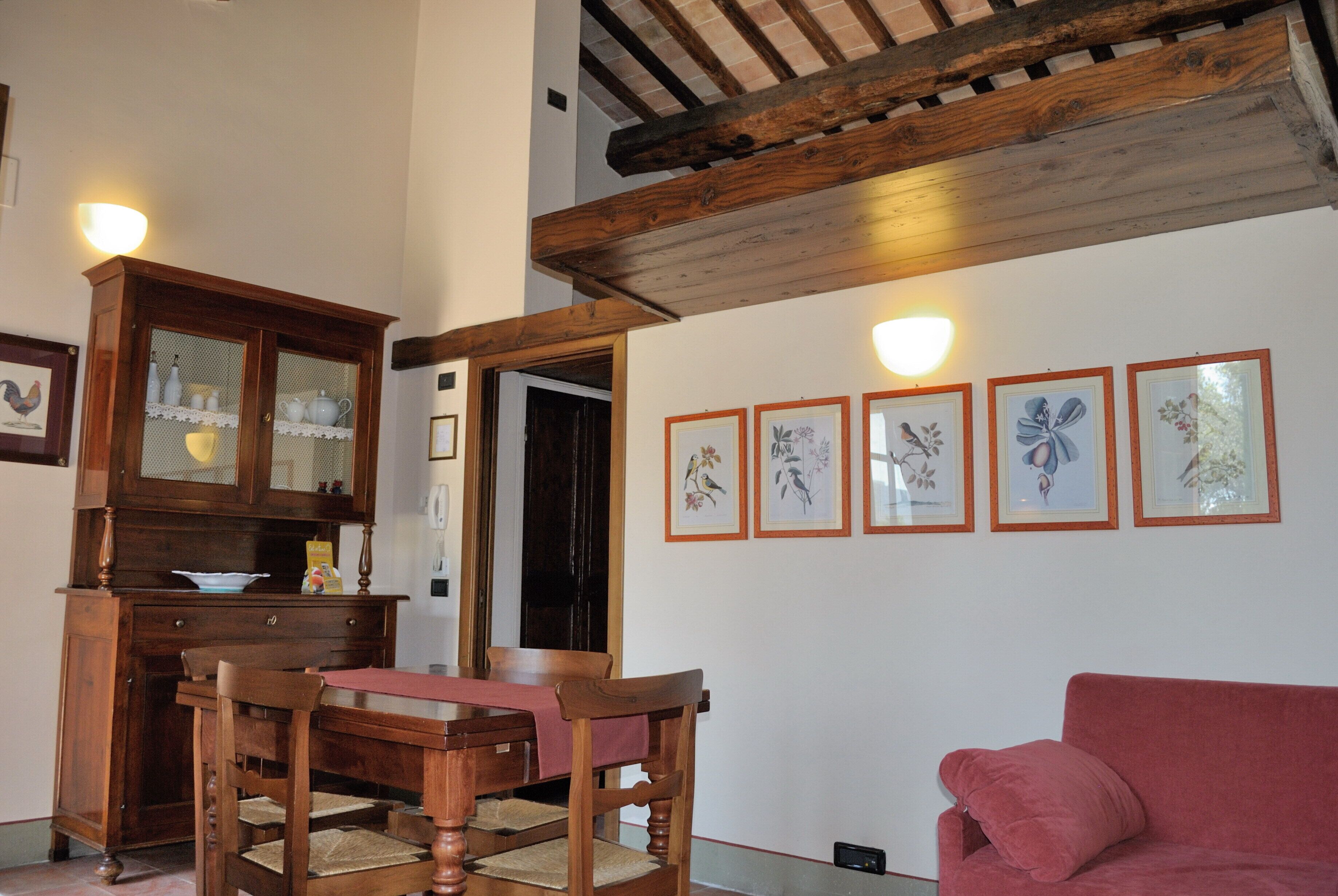 A dining area with wooden furniture, a red couch, and framed floral artwork on the wall.