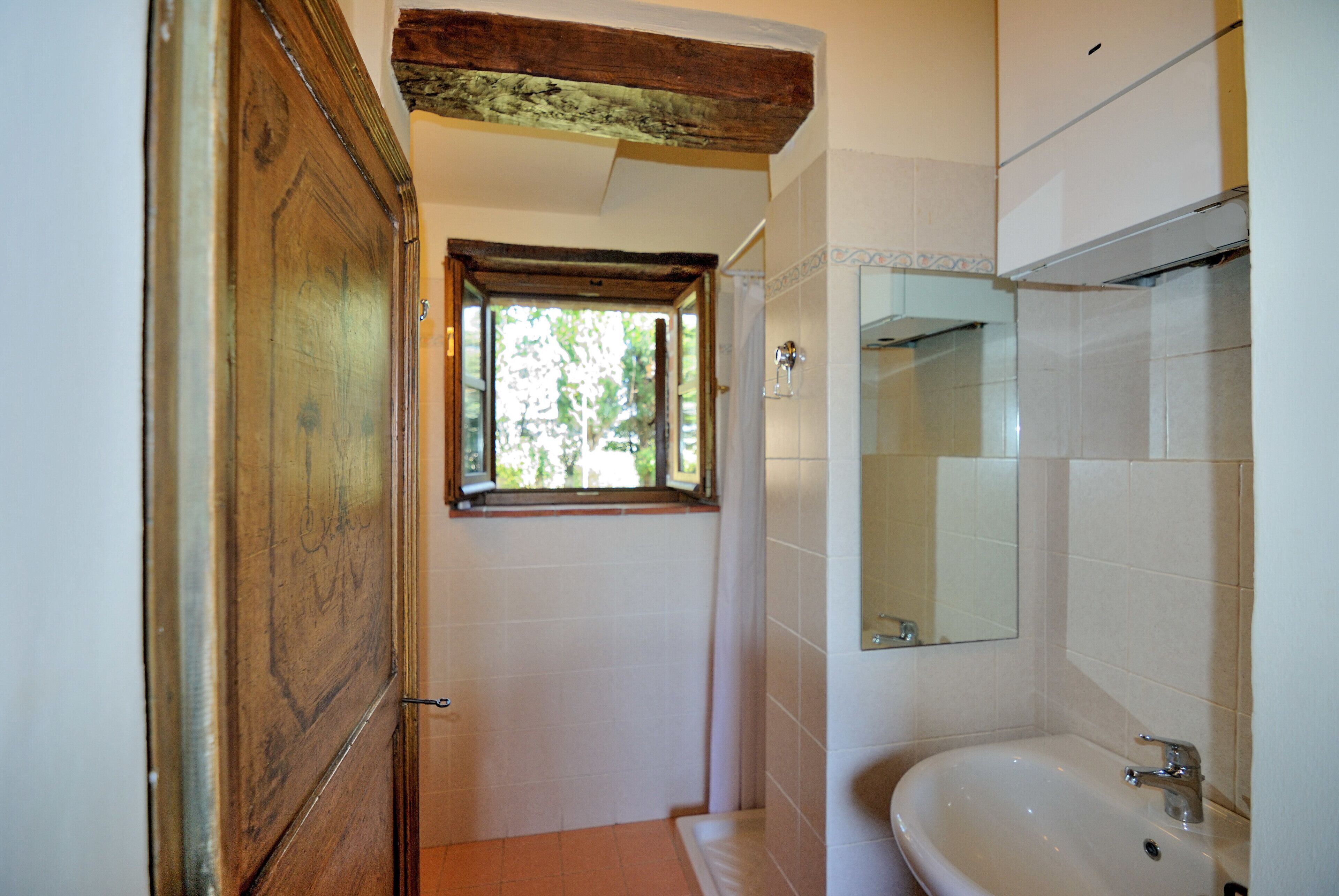 A bathroom with a wooden door, a window, a sink, and a mirror.