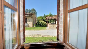 Uitzicht vanuit een raam op een binnenplaats met stenen gebouwen, een pergola en een helderblauwe lucht.