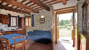Una cocina rústica con paredes de piedra, vigas de madera, un sofá azul y una mesa de comedor con sillas.
