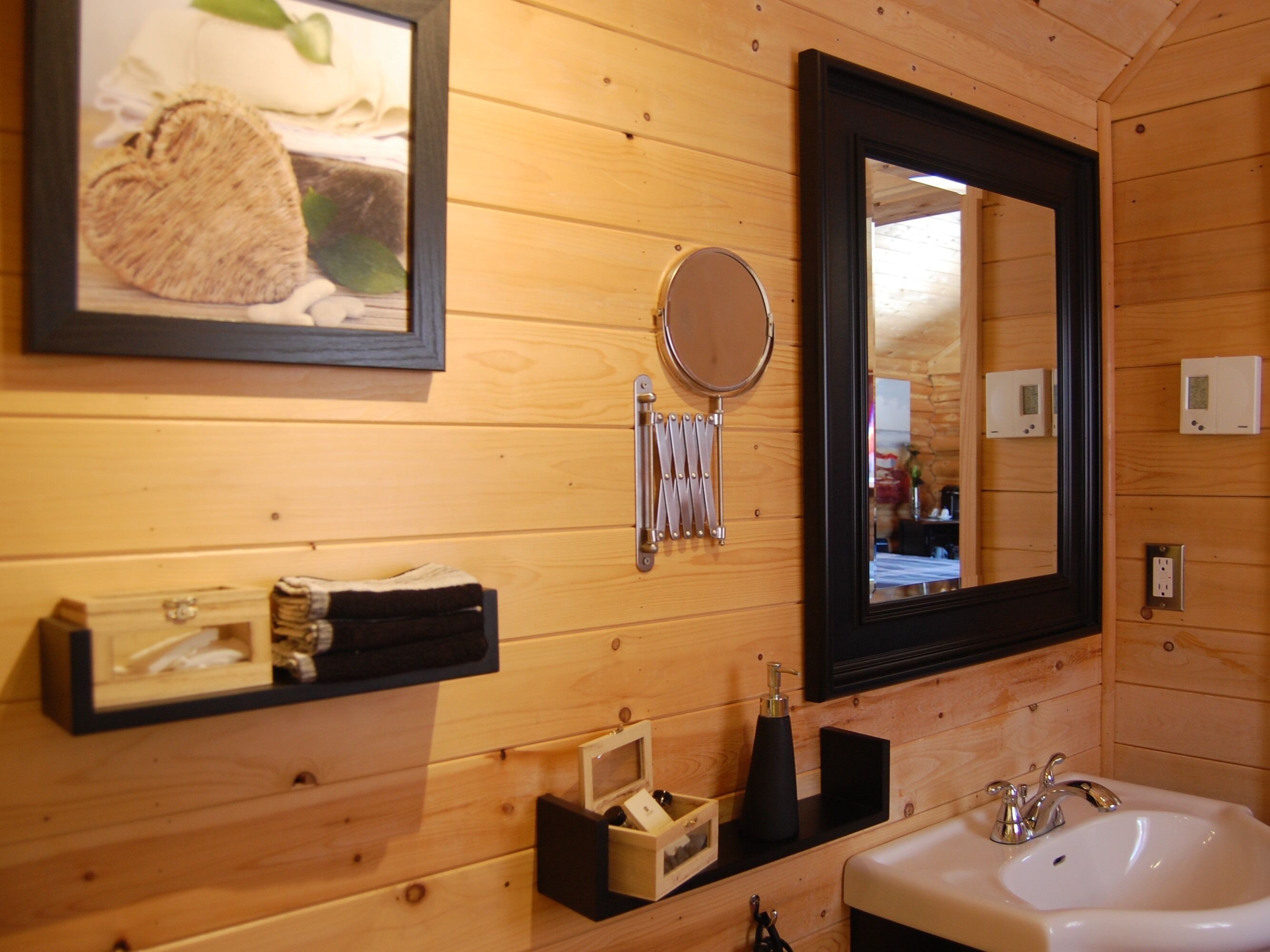 Une salle de bain en bois avec un lavabo, un miroir, un porte-serviettes et un tableau encadré.