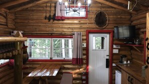 A log cabin interior with a wooden ceiling, a dining table, a television, and a small kitchenette. - Domaine le Bostonnais (La Bostonnais)