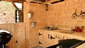 A rustic wooden cabin with a stone wall, wooden cabinets, a sink, and a grill. - Domaine le Bostonnais (La Bostonnais)