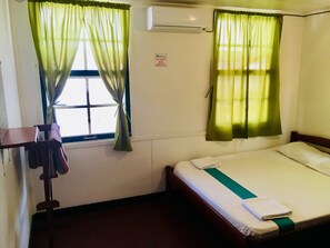 A hotel room with a bed, a window with curtains, an air conditioning unit, and a towel rack. - Guesthouse De Kleine Historie (Paramaribo)