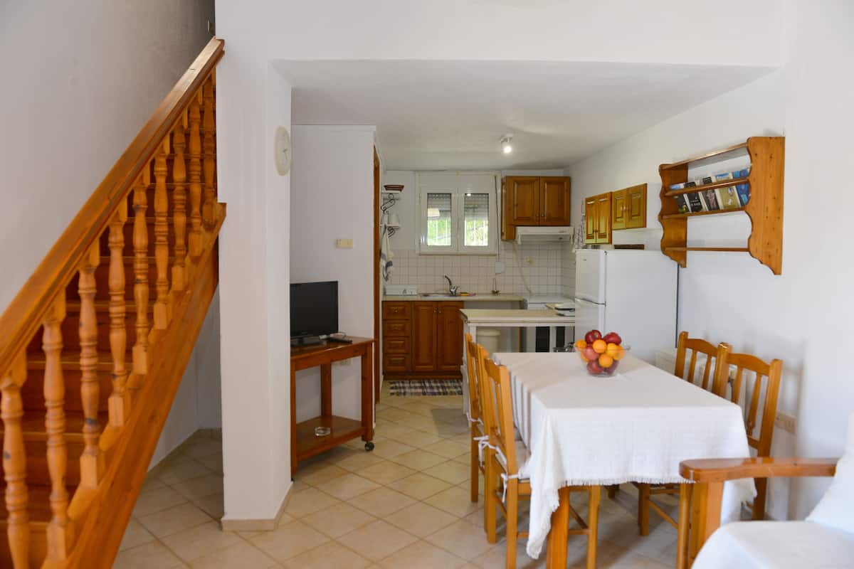 A kitchen with wooden cabinets, a dining table with chairs, a TV on a stand, and a fruit bowl on the table.