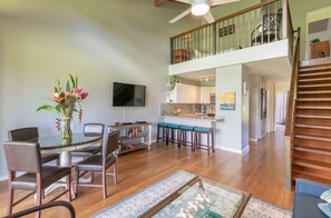 Relax in this spacious living area with a high ceiling, featuring a round table, comfortable seating, and a flat-screen TV.