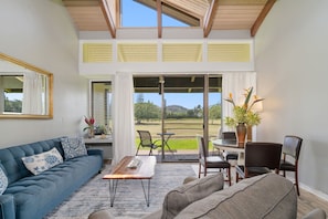 Relax in this spacious living room with a sofa, coffee table, and dining area leading to a patio with a scenic view.