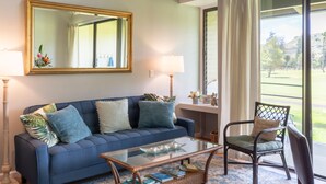 Un salon avec un canapé bleu, une table basse en verre, un fauteuil, un grand miroir et une vue sur un terrain de golf, visible à travers de grandes fenêtres.