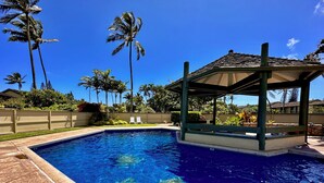 Une piscine à l’eau d’un bleu cristallin, entourée de palmiers et abritée par un pavillon.