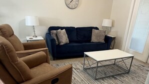 A living room with a brown armchair, a blue sofa, a white coffee table, and a wall clock.