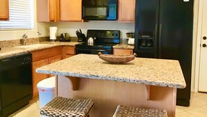 A kitchen with wooden cabinets, a granite countertop, a black refrigerator, a microwave, a stove, and a sink.
